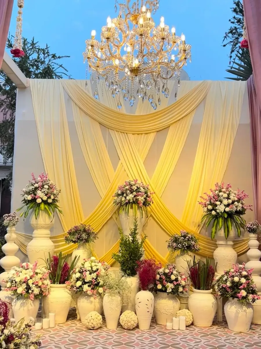 Gold and ivory draped ceremony backdrop with a crystal chandelier and flower urns