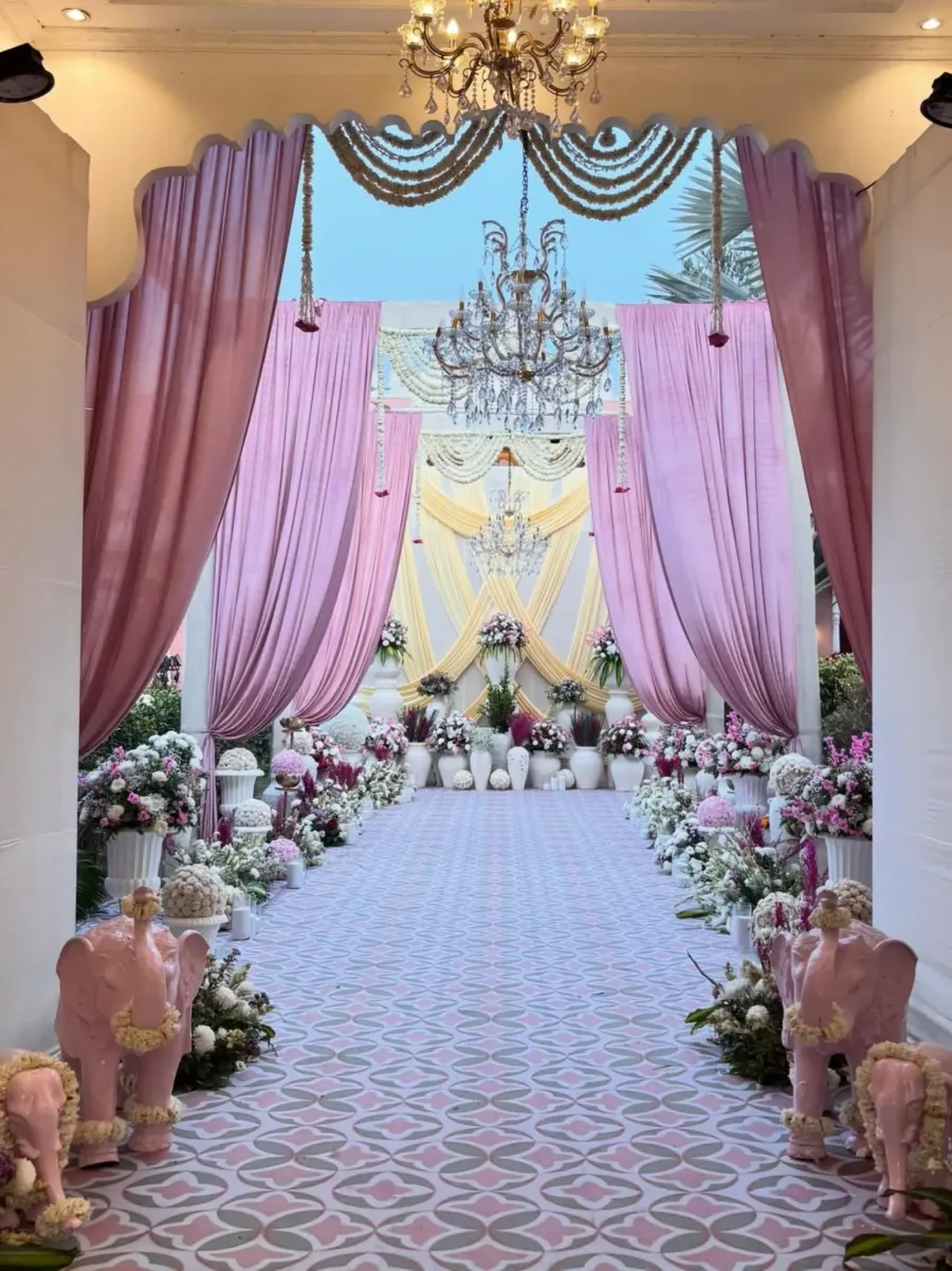 Draped entrance walkway in blush and lilac, chandeliers overhead and a floral aisle