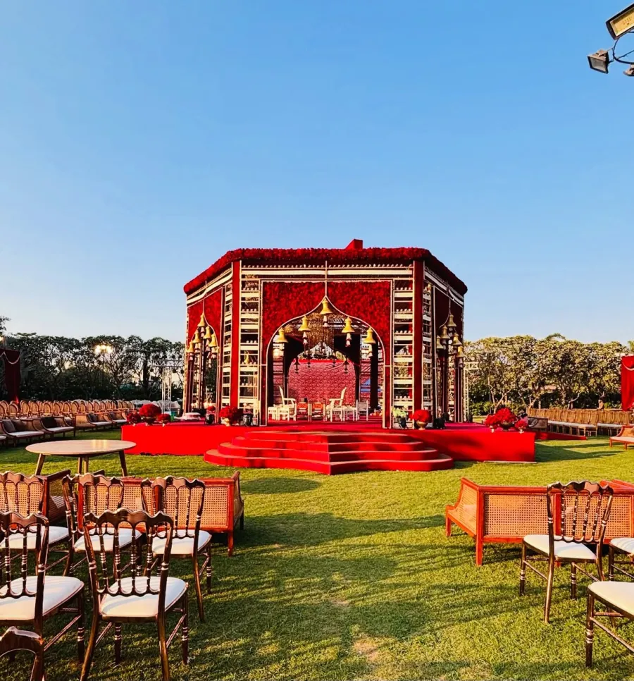 Ornate red and gold pavilion mandap on a lawn under a clear sky